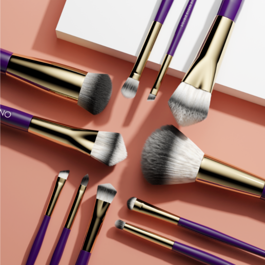 Assortment of makeup brushes with purple handles and gold accents on a white and a peach-colored surface.
