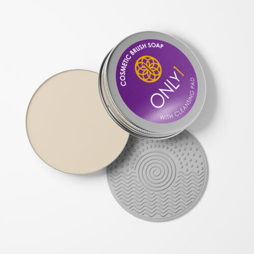 Cosmetic brush soap with a cleansing pad in an open tin container. The tin has a purple lid, and the cleansing pad features a textured gray surface with spiral and wave patterns. The background is plain white.