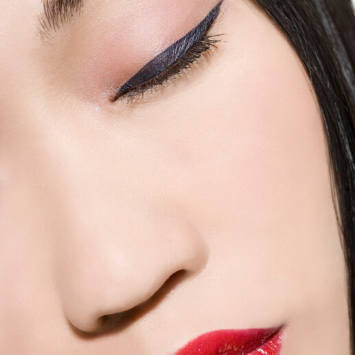 Woman with closed eyes, winged eyeliner, and red lipstick. She has straight, dark hair.