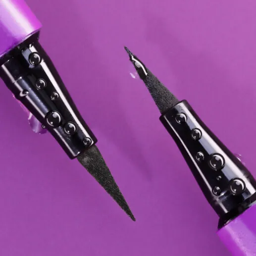 Two liquid eyeliner pens with fine black tips and purple casings, on a purple background.