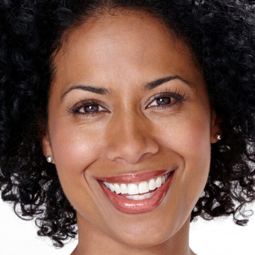 Smiling woman with curly hair, natural makeup, and glossy lips.