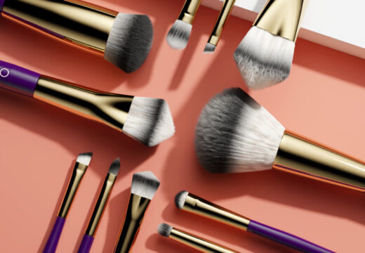 Assortment of makeup brushes with purple handles and gold accents on a peach-colored surface.